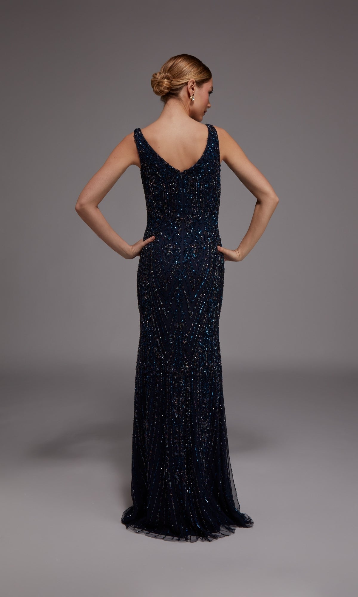 A woman faces away in a studio, wearing the Alyce 27786—an elegant, floor-length navy blue formal dress with intricate beadwork and a sleeveless design.